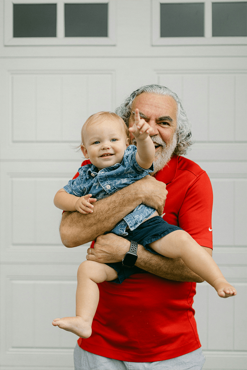 Grandfather in a red shirt holding his toddler grandchild. 