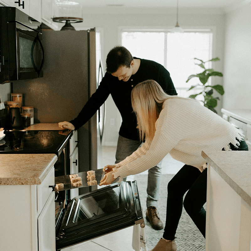 A man and a woman placing a sheet of cookies into an oven.