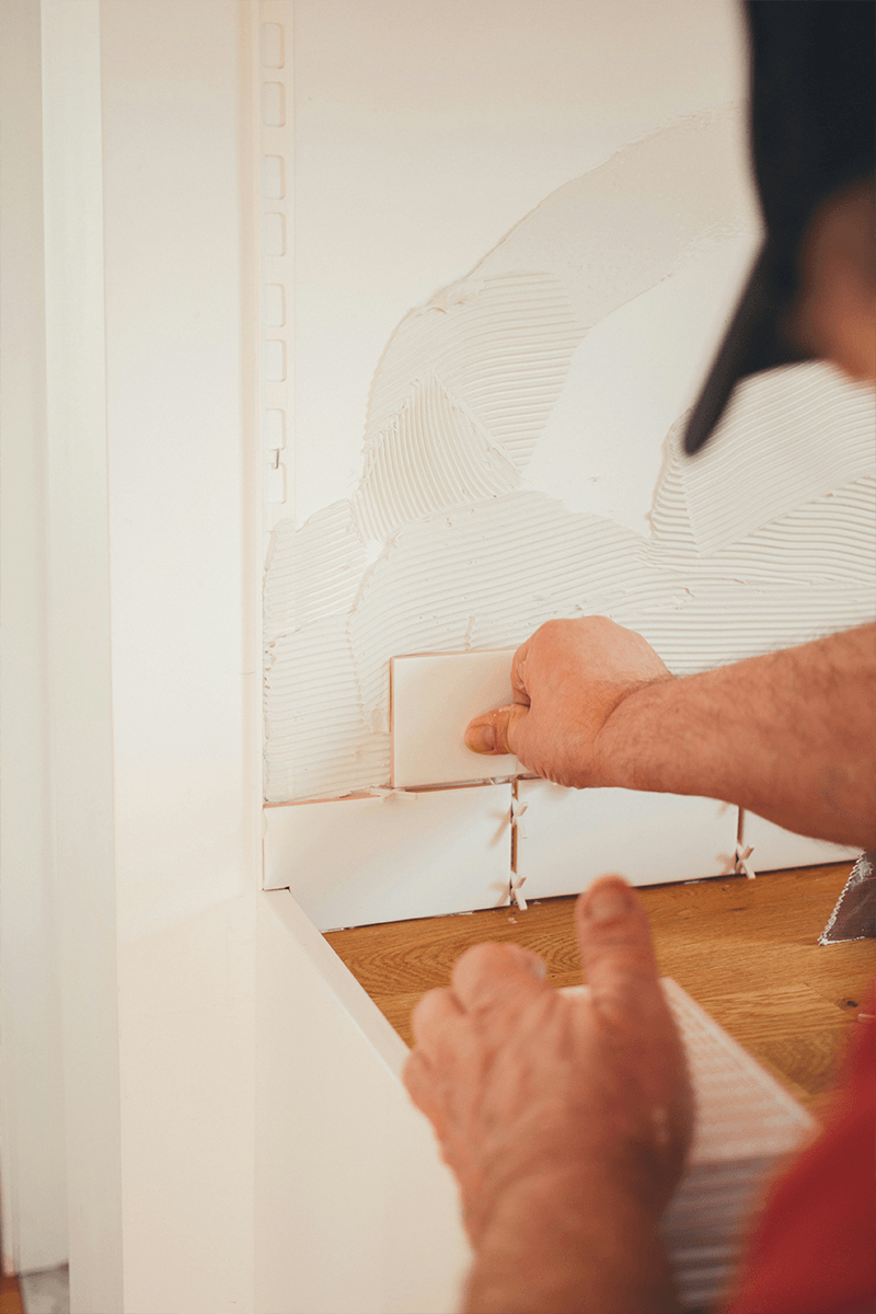 Man in a red shirt and a black hat installing white tile. 