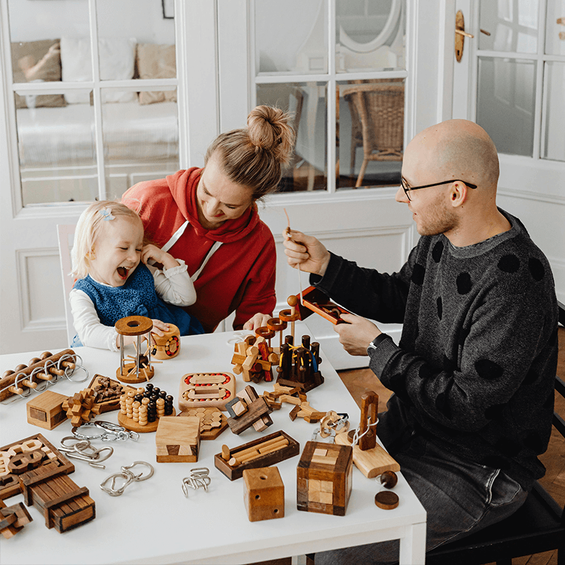 A husband and wife playing with their young daughter with wooden toys.