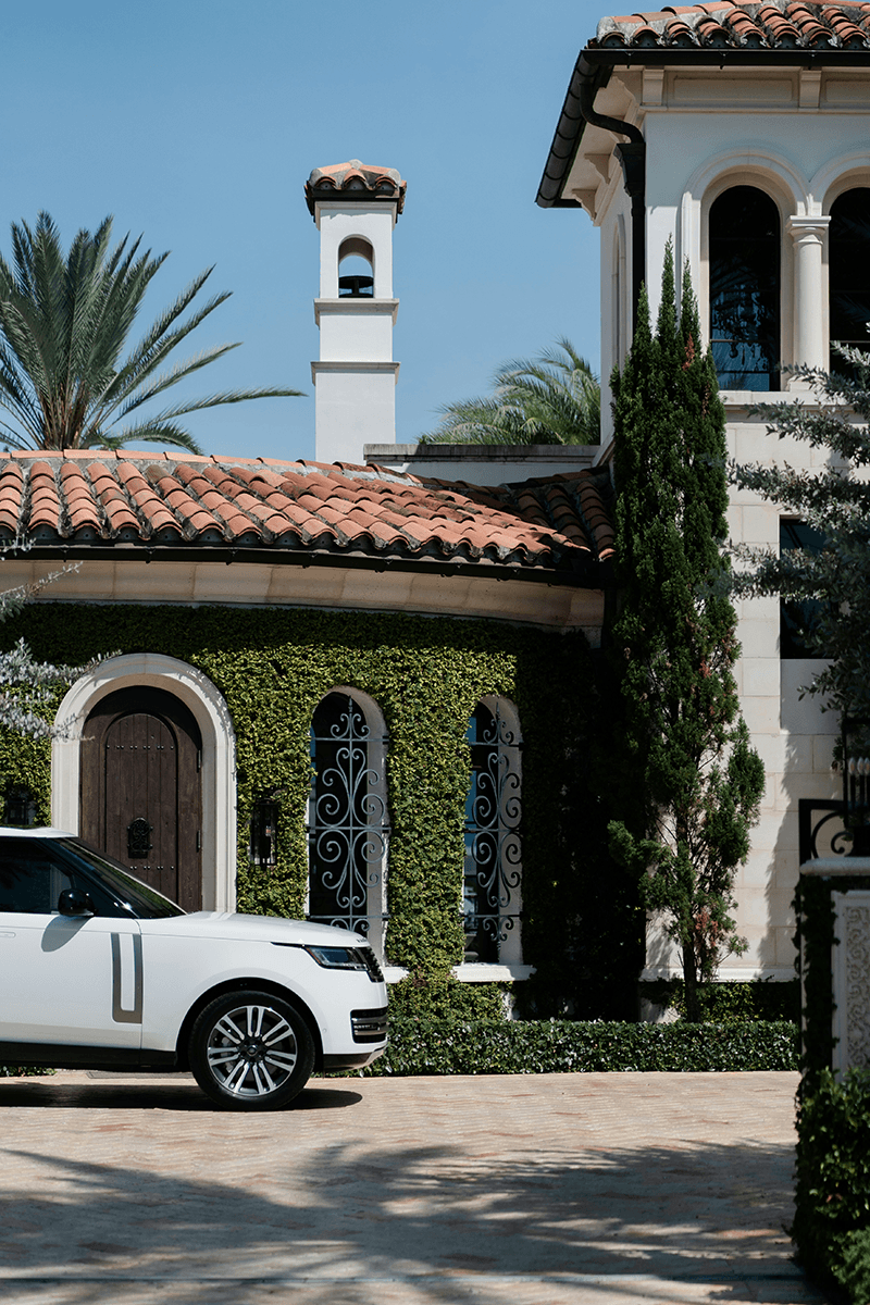 White suv parched infront of a Spanish style home. 