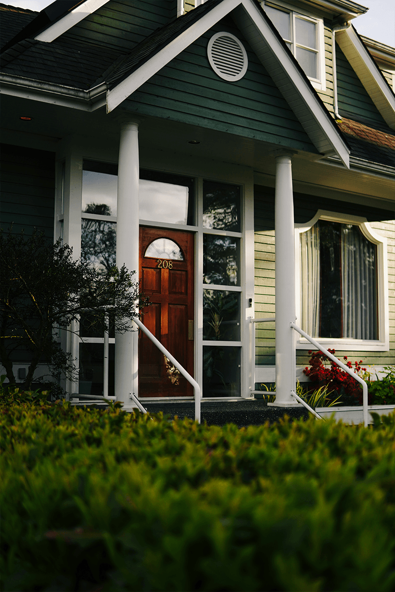 A well-maintained house with a red front door, and two colors of green siding